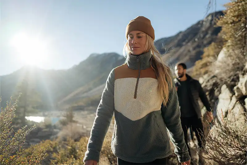 Two people hiking on a mountainous  trail, with the woman in the foreground wearing a Prism Half-Zip Fleece from Kuhl