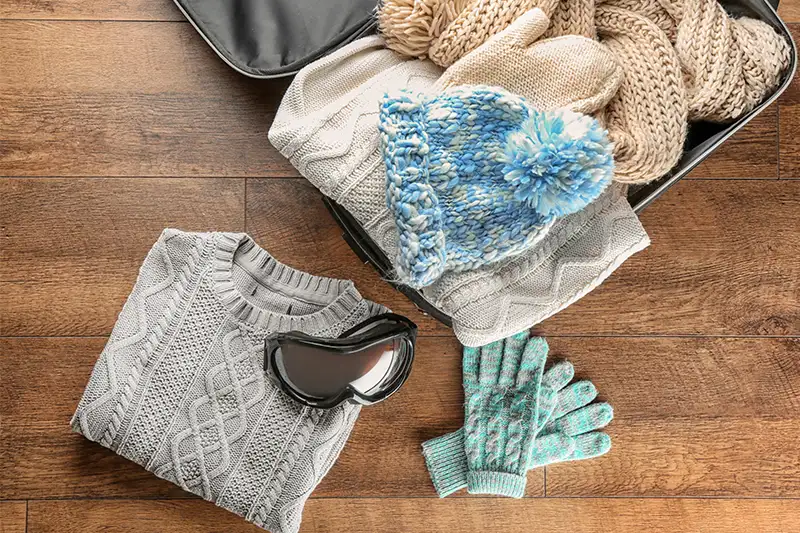 An open suitcase full of winter clothes on a wood floor backdrop