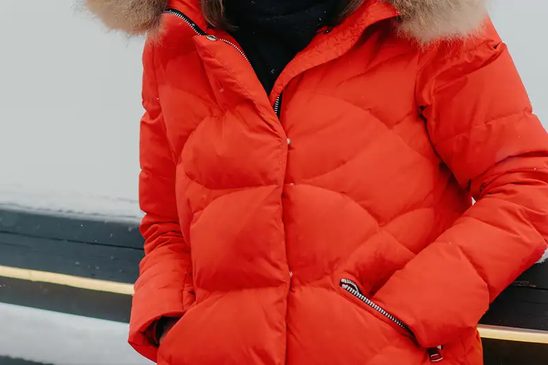 Close up of person putting their hand inside the pocket of a red ski jacket