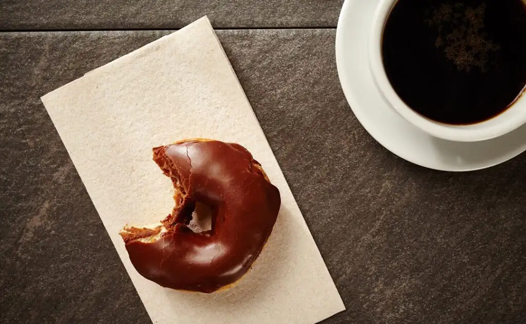 Donut with a bight taken with a black coffee.
