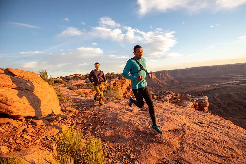 Two people jogging on a desert nature trail wearing the Janji Transit Tech Pants