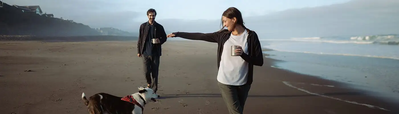 Couple walking along the beach with their dog wearing the Frost Pant from Kuhl