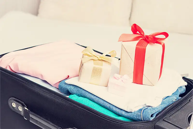 Three wrapped gifts sitting on top of packed suitcase