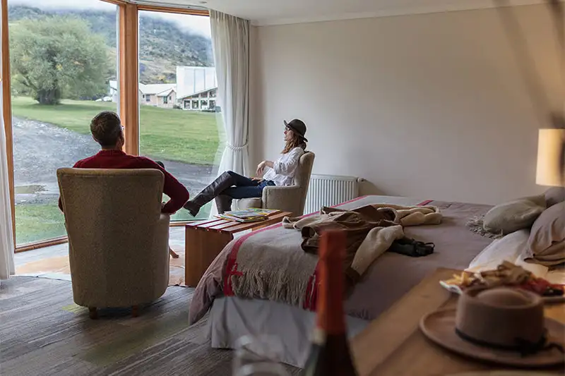 Couple relaxing in guest room, looking out large glass door, at Las Torres Patagonia Hotel