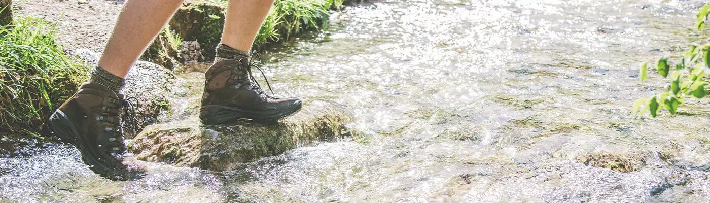 Man crossing river while hiking in waterproof leather shoes
