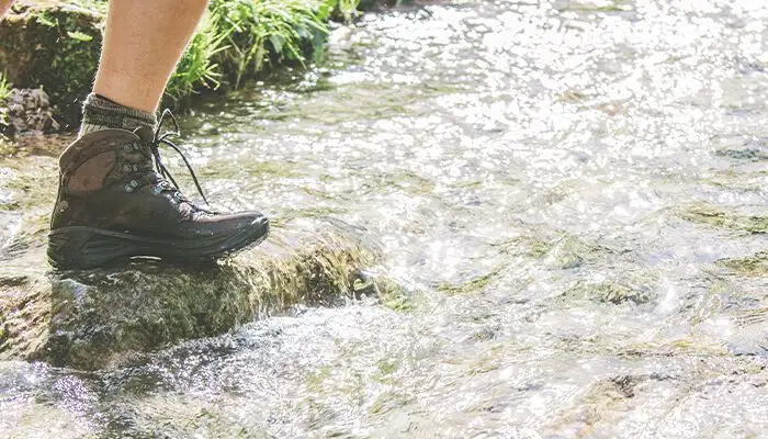 Man crossing river while hiking in waterproof leather shoes