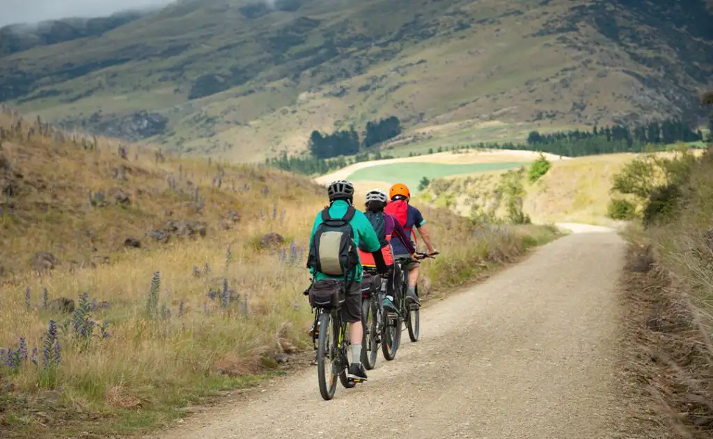 Three people cycling the Otago Central Rail Trail in a row towards Middlemarch, South Island, New Zealand