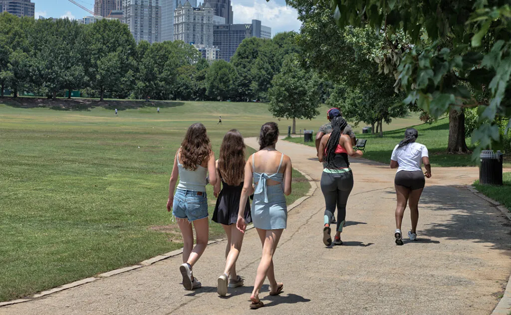 Unidentifiable walkers and runners on a path at Piedmont Park in Atlanta, GA on a hot summer day with buildings in the distance
