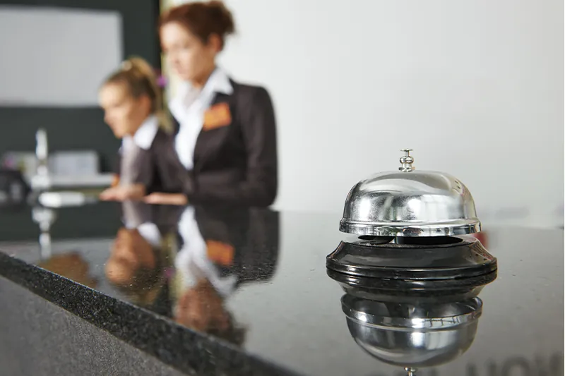 Silver bell on front desk of hotel, with front desk workers out-of-focus in the background