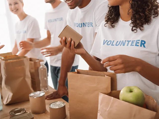 Close up of volunteers packing lunches in brown paper bags